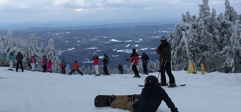 View from the top of Mount Snow with several skiers and a snowboarder spread out across the top of the trail
